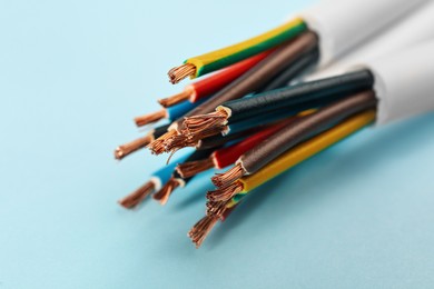 Photo of Cables with stripped electrical wires on light blue background, closeup