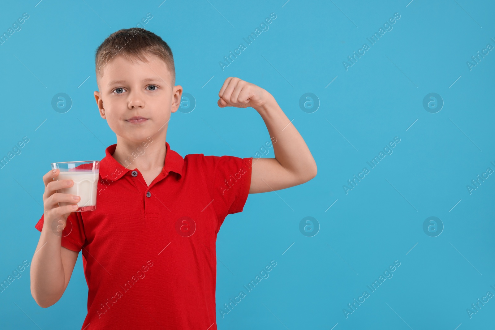 Photo of Cute boy with glass of fresh milk showing his strength on light blue background, space for text