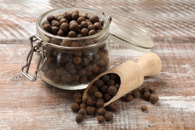Photo of Aromatic allspice pepper grains in glass jar and scoop on wooden table