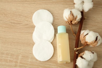 Photo of Cosmetic product, cotton pads and flowers on wooden table, flat lay. Space for text