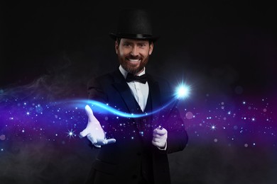 Image of Smiling magician showing trick with wand on black background