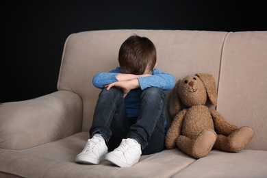 Sad little boy with toy sitting on couch at home