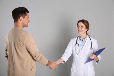 Photo of Doctor and patient shaking hands on light grey background