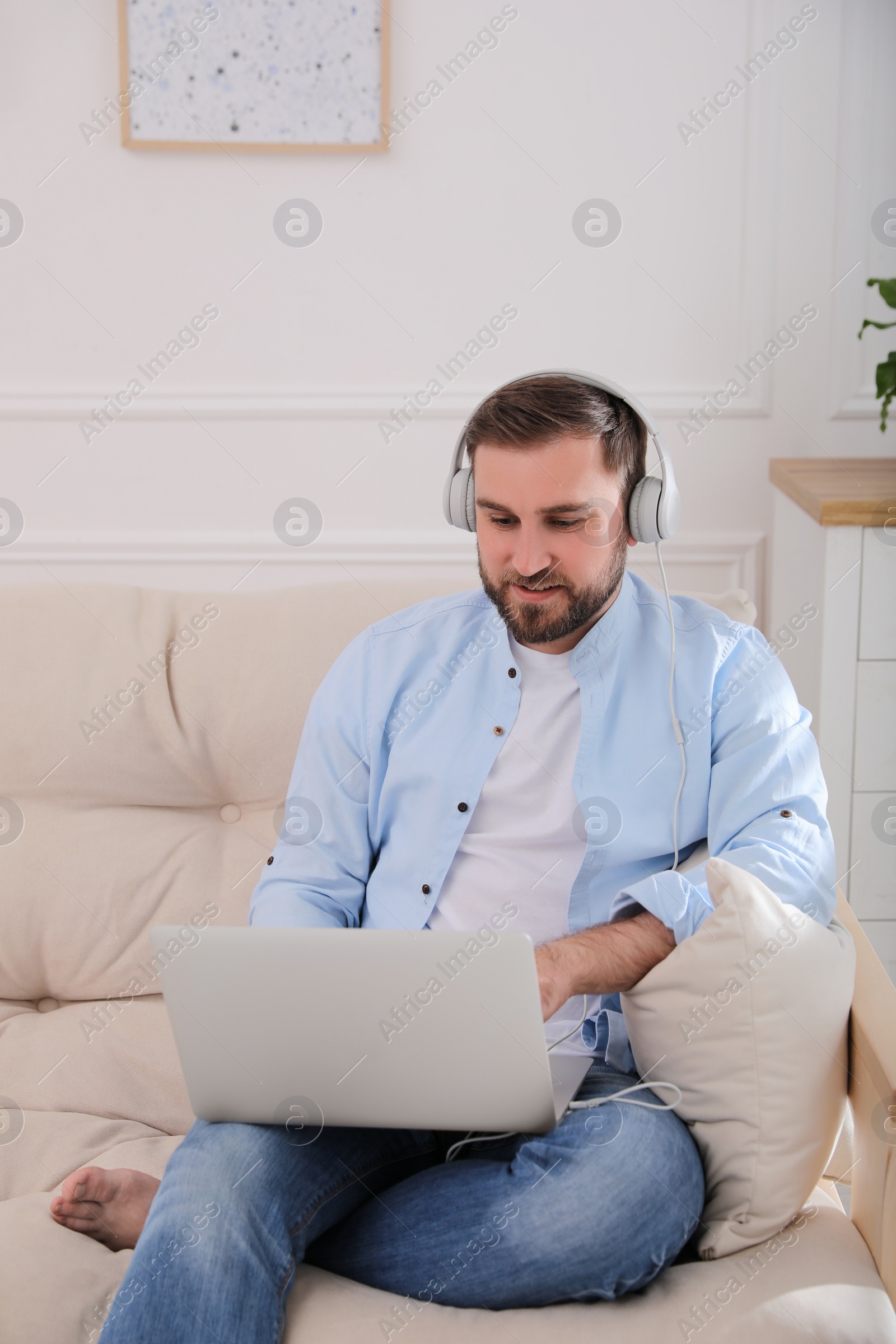 Photo of Man with laptop and headphones sitting on sofa at home