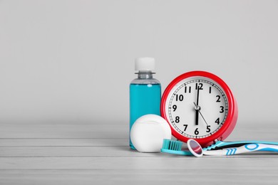 Photo of Composition with dental floss, alarm clock and different teeth care products on white wooden table. Space for text
