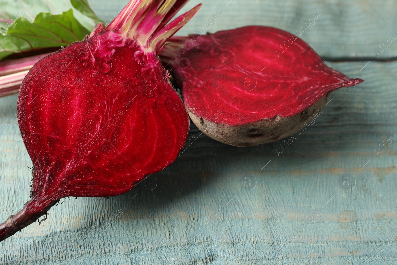 Photo of Halves of raw beet on blue wooden table, closeup