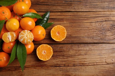Photo of Fresh tangerines with green leaves on wooden table, top view. Space for text