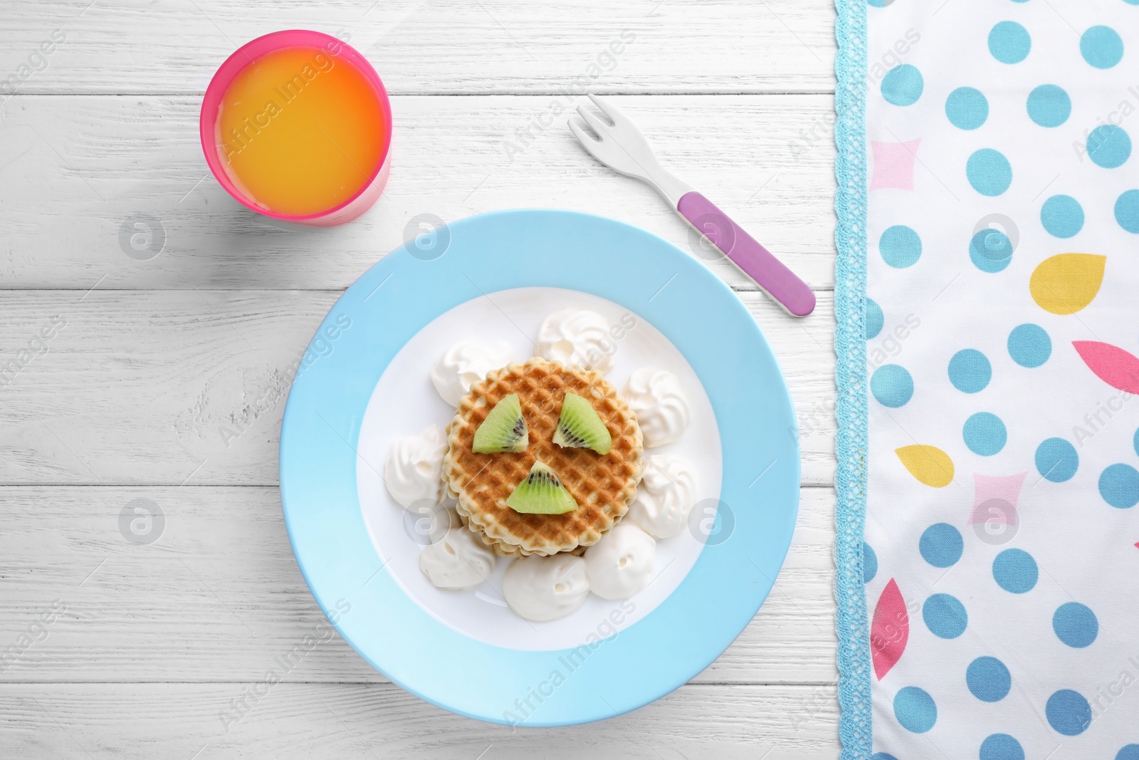 Photo of Tasty waffles served with whipped cream and juice on white wooden table, flat lay. Creative idea for kids breakfast