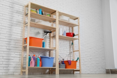 Photo of Wooden shelving units with cleaning equipment near white brick wall. Stylish room interior