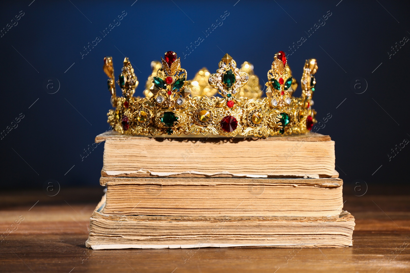 Photo of Beautiful golden crown on old books against dark blue background. Fantasy item