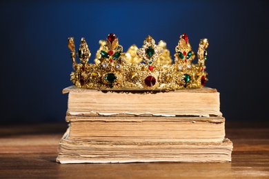 Beautiful golden crown on old books against dark blue background. Fantasy item