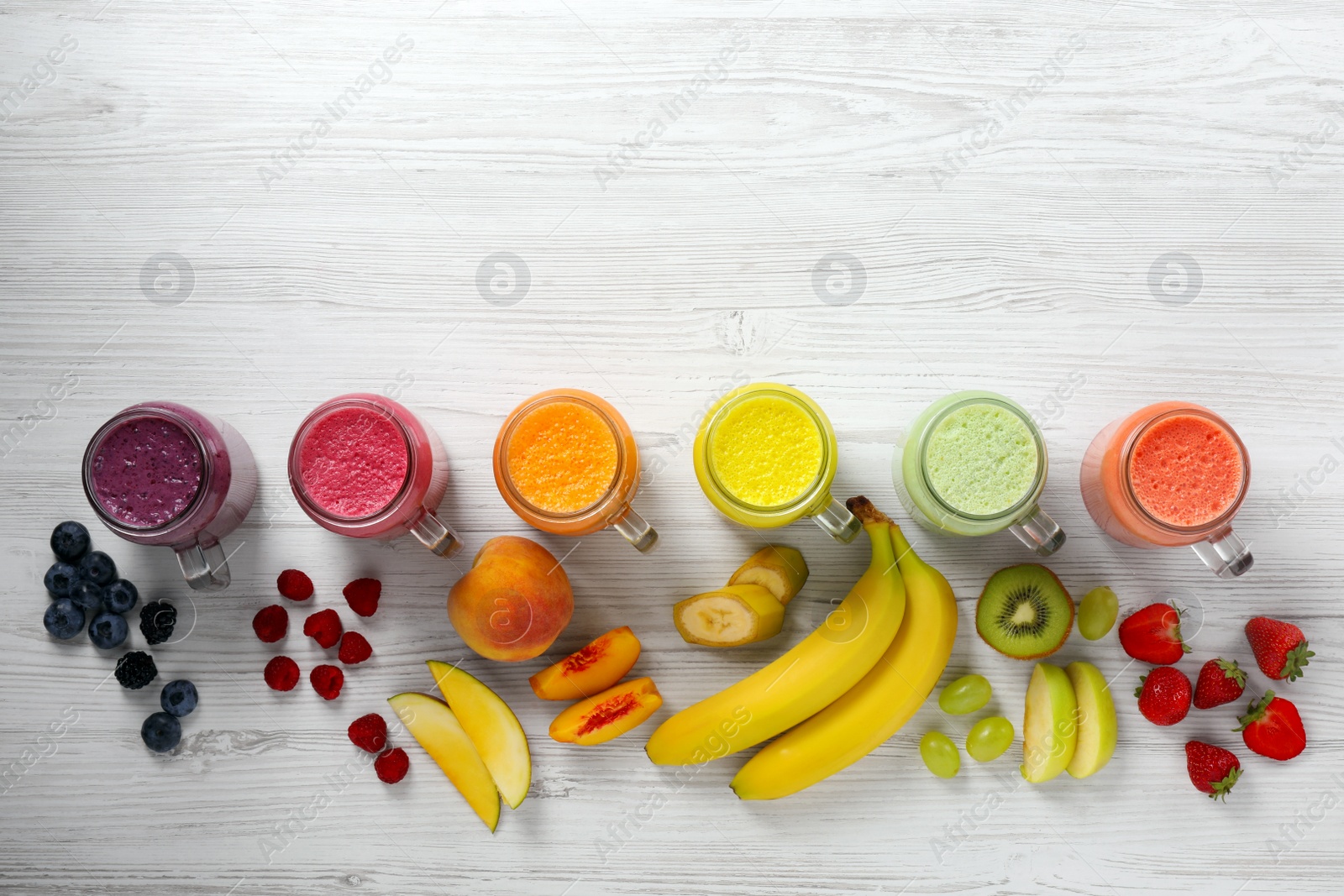 Photo of Many different tasty smoothies and ingredients on white wooden table, flat lay. Space for text