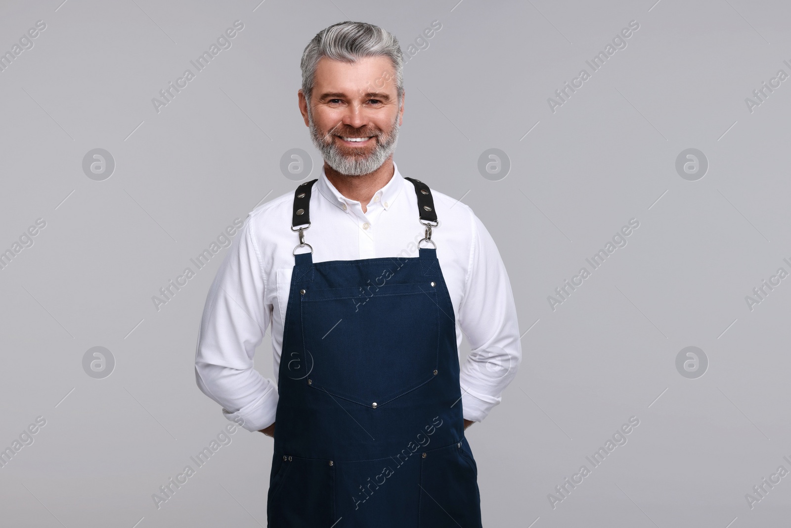 Photo of Happy man wearing kitchen apron on grey background. Mockup for design