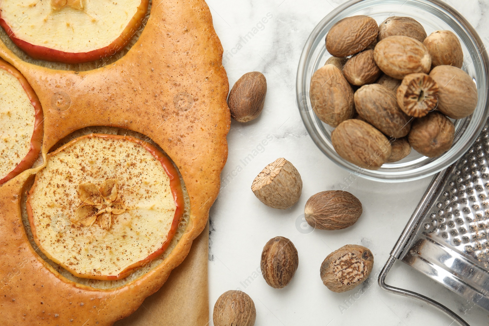 Photo of Nutmeg seeds, grater and tasty apple pie on white marble table, flat lay