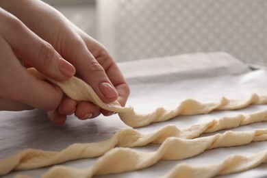 Photo of Woman putting homemade breadsticks on baking sheet indoors, closeup. Cooking traditional grissini