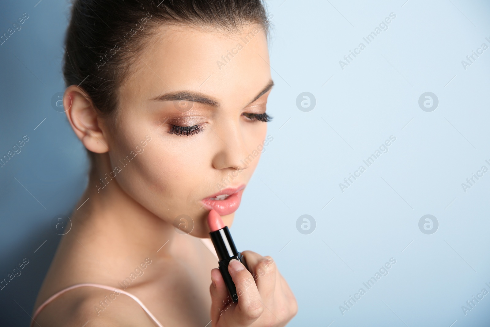 Photo of Young woman applying lipstick on color background. Professional makeup products