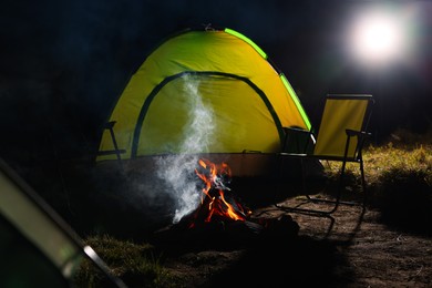 Photo of Beautiful bonfire and folding chairs near camping tent outdoors at night