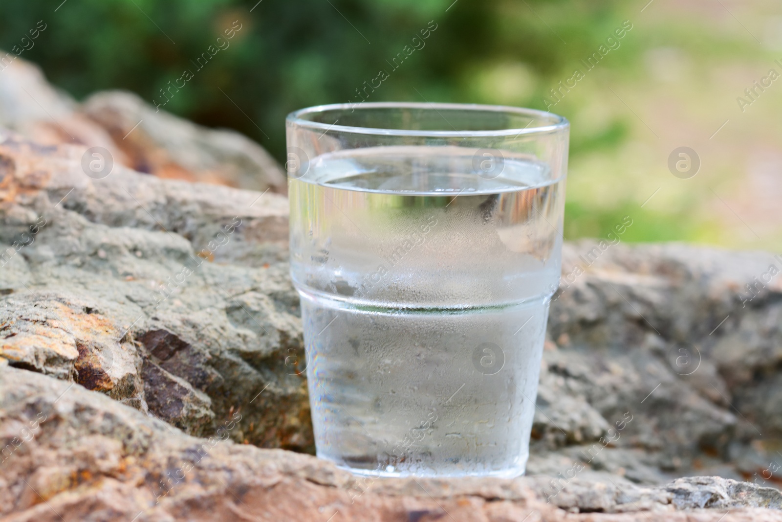 Photo of Glass of cool water on stone outdoors, closeup