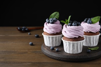 Sweet cupcakes with fresh blueberries on wooden table. Space for text