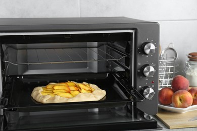 Photo of Open electric oven with uncooked pie on countertop in kitchen