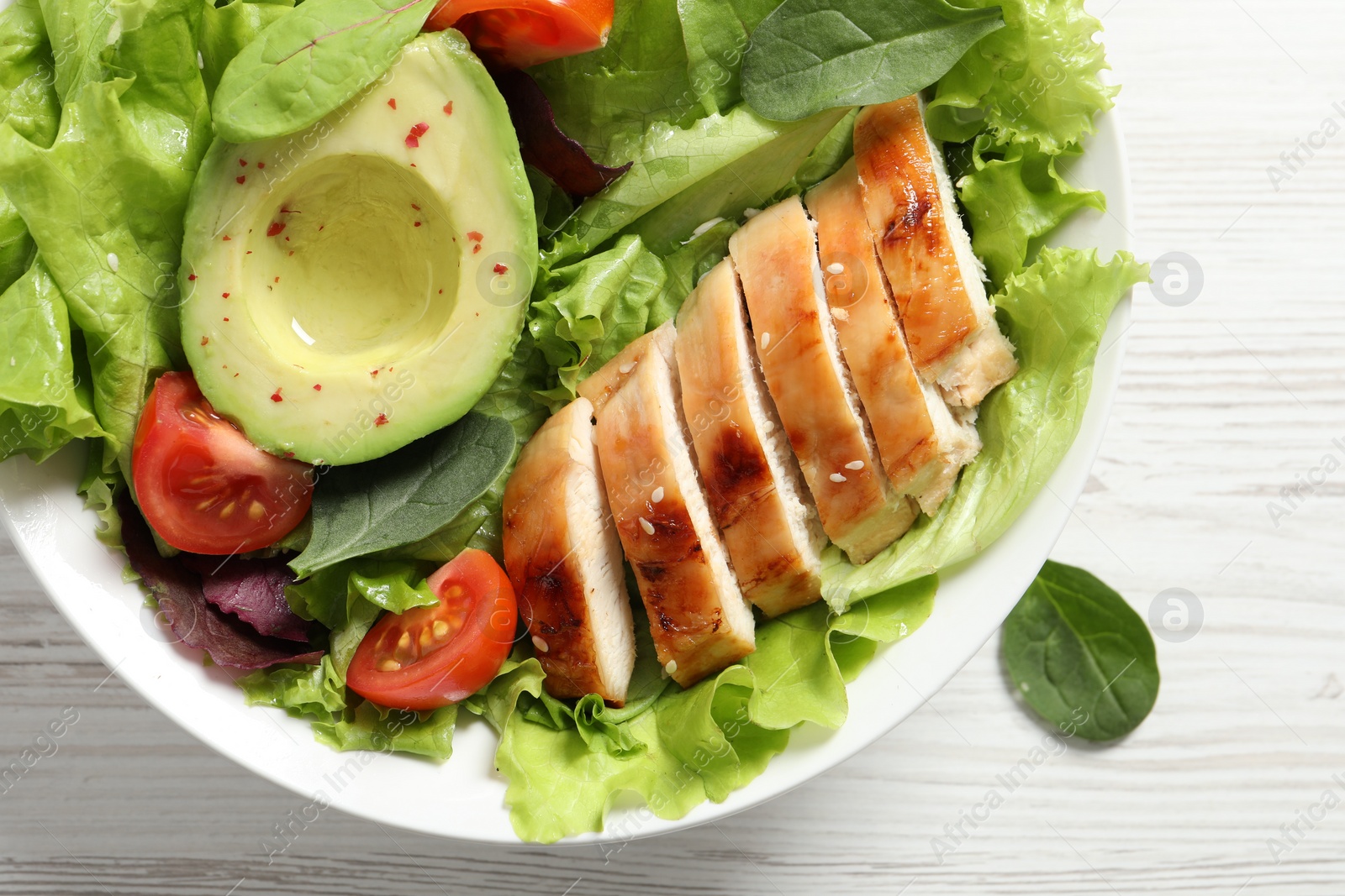 Photo of Delicious salad with chicken, cherry tomato and avocado on white wooden table, top view