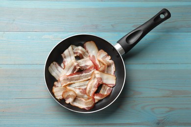 Delicious bacon slices in frying pan on light blue wooden table, top view