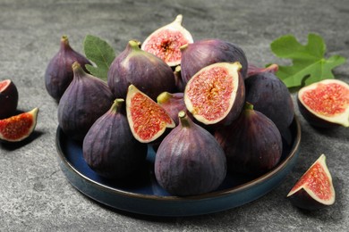 Photo of Whole and cut ripe figs on light grey textured table, closeup