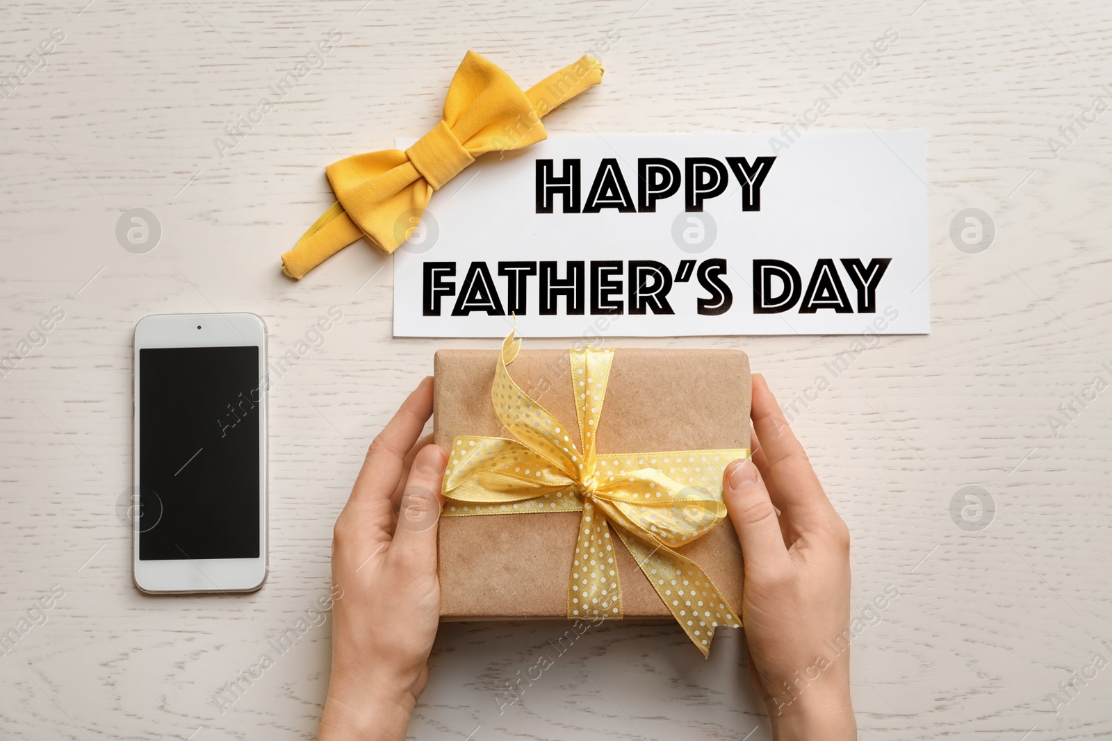 Photo of Man holding gift box near smartphone and bow tie on table, top view. Father's day celebration