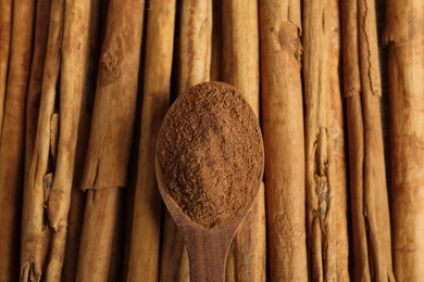 Photo of Wooden spoon with aromatic cinnamon powder over sticks, top view