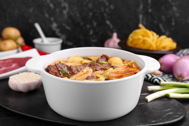 Photo of Pot of delicious vegetable soup with meat, noodles and ingredients on black wooden table