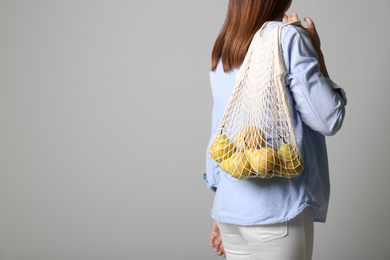 Photo of Woman holding net bag with fresh ripe pears on grey background, closeup. Space for text