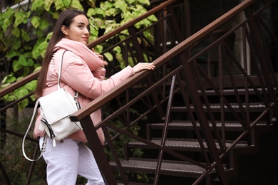 Photo of Young female traveler with stylish backpack going upstairs outdoors