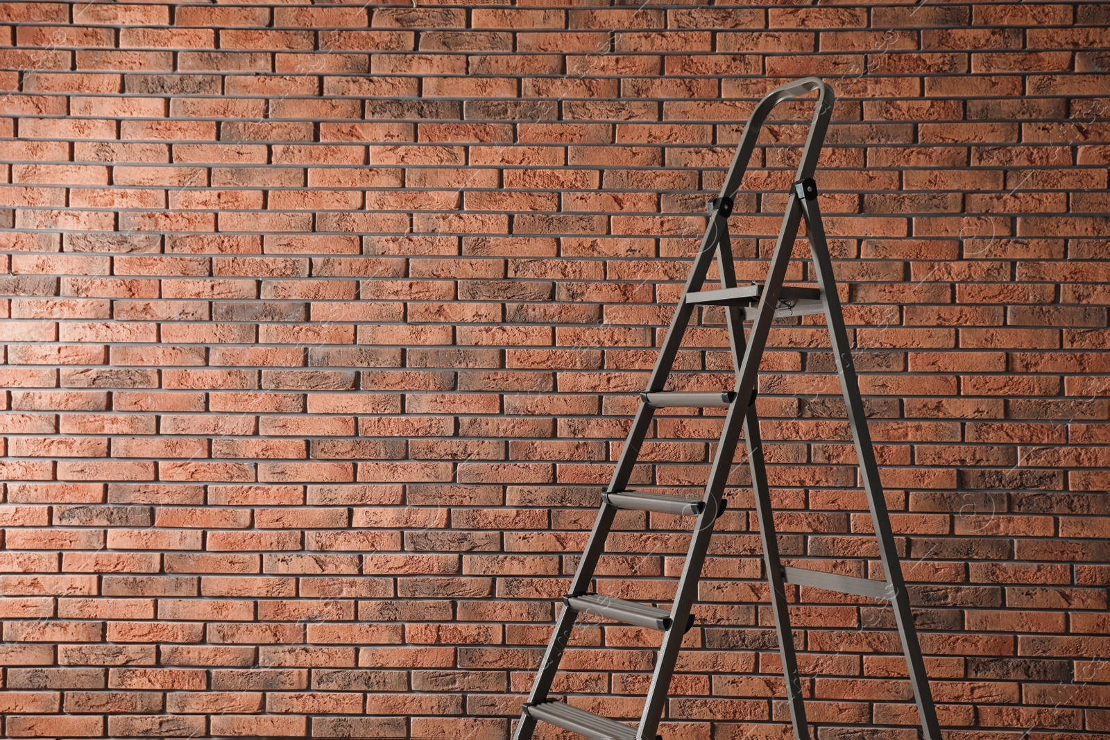 Photo of Metal stepladder near brick wall. Space for text