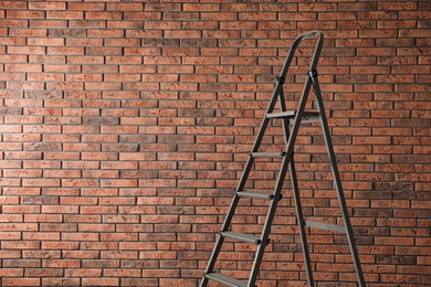 Photo of Metal stepladder near brick wall. Space for text