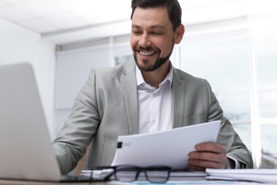 Businessman working with laptop and documents at table in office