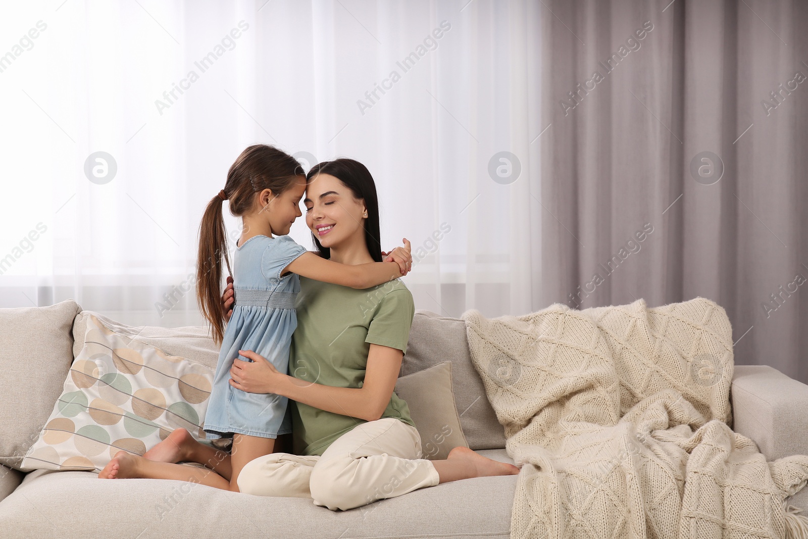 Photo of Happy woman and her cute daughter spending time together on sofa at home. Mother's day celebration