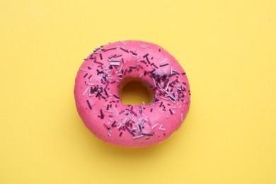 Photo of Glazed donut decorated with sprinkles on yellow background, top view. Tasty confectionery