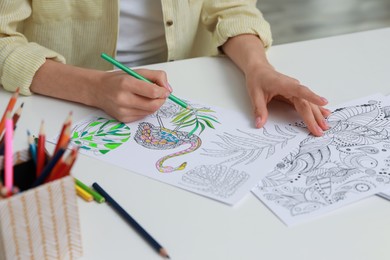 Young woman coloring antistress page at table indoors, closeup