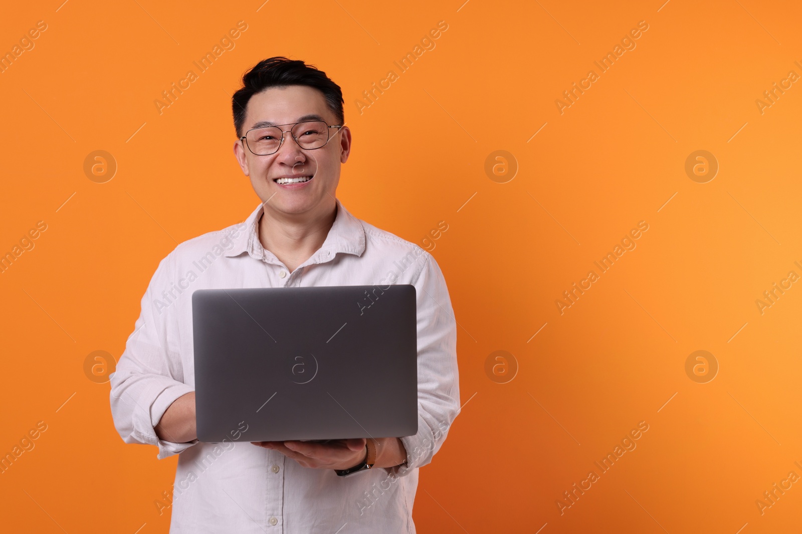Photo of Happy man with laptop on orange background, space for text