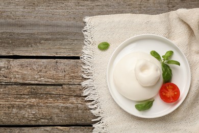 Photo of Delicious burrata cheese with basil and tomato on wooden table, top view. Space for text