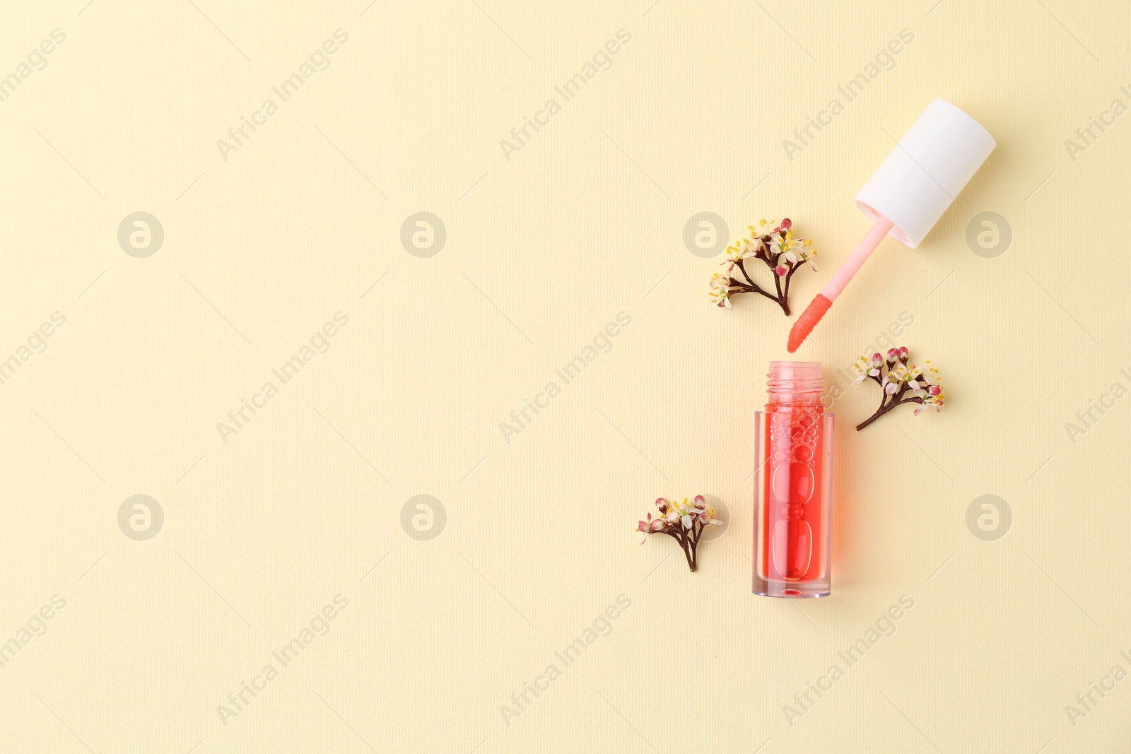Photo of Bright lip gloss, applicator and flowers on yellow background, top view. Space for text