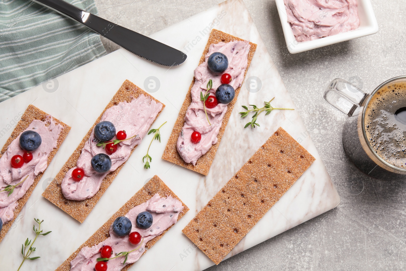 Photo of Tasty cracker sandwiches with cream cheese, blueberries, red currants, thyme and cup of coffee on grey table, flat lay