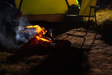 Photo of Man sitting near bonfire and camping tent at night