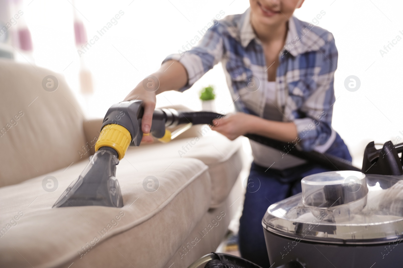 Photo of Woman removing dirt from sofa with vacuum cleaner at home, closeup