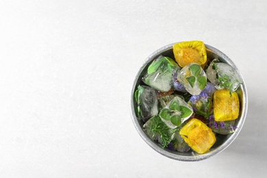 Bucket of ice cubes with flowers on light background, top view. Space for text