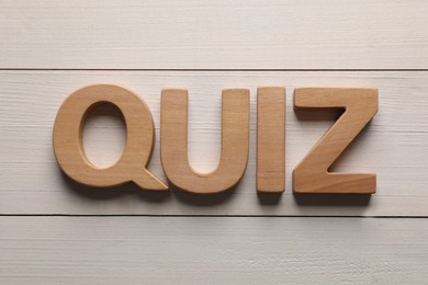 Photo of Word Quiz made with wooden letters on white table, flat lay