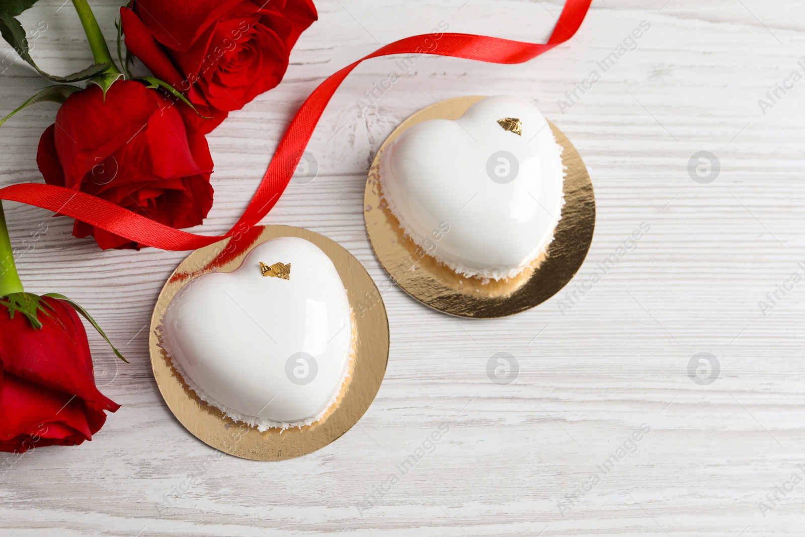 Photo of St. Valentine's Day. Delicious heart shaped cakes and roses on white wooden table, flat lay. Space for text