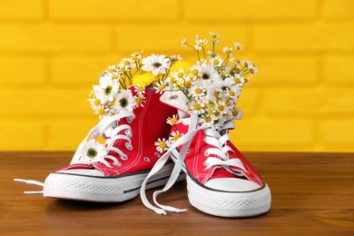 Shoes with beautiful flowers on wooden surface against yellow brick wall