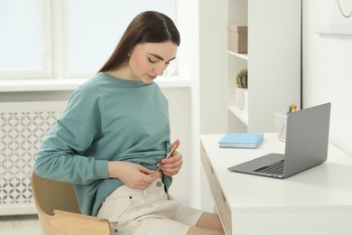 Diabetes. Woman making insulin injection into her belly at table indoors