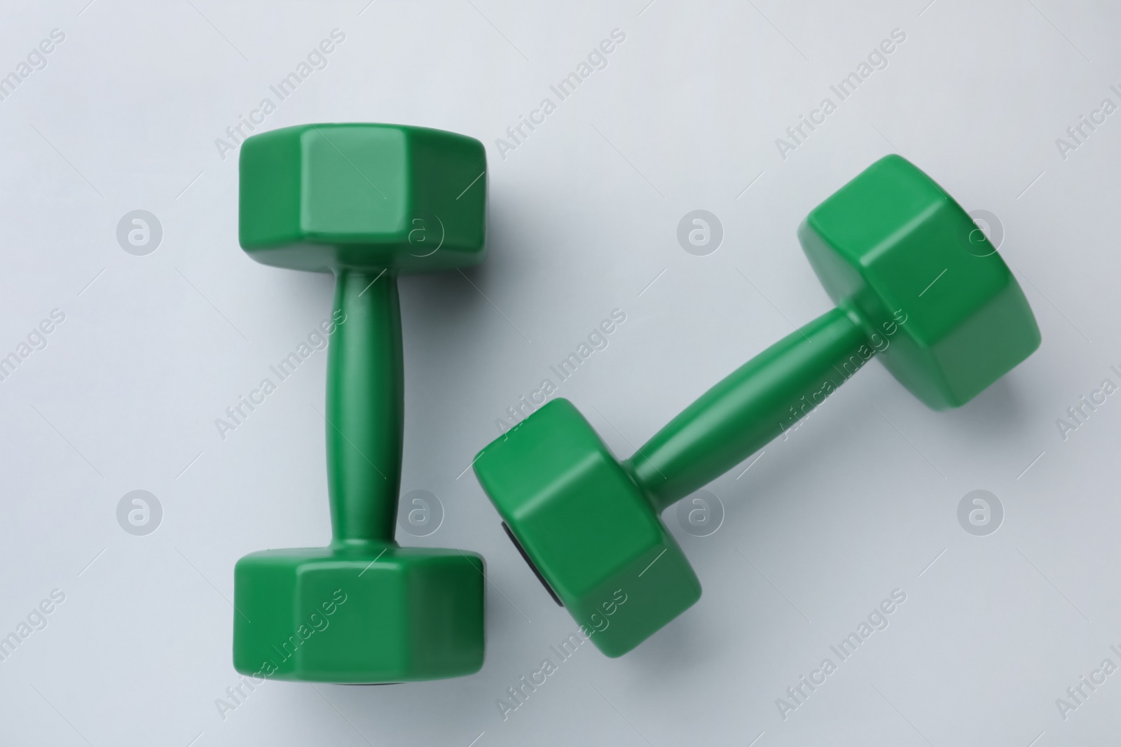 Photo of Green vinyl dumbbells on light background, flat lay